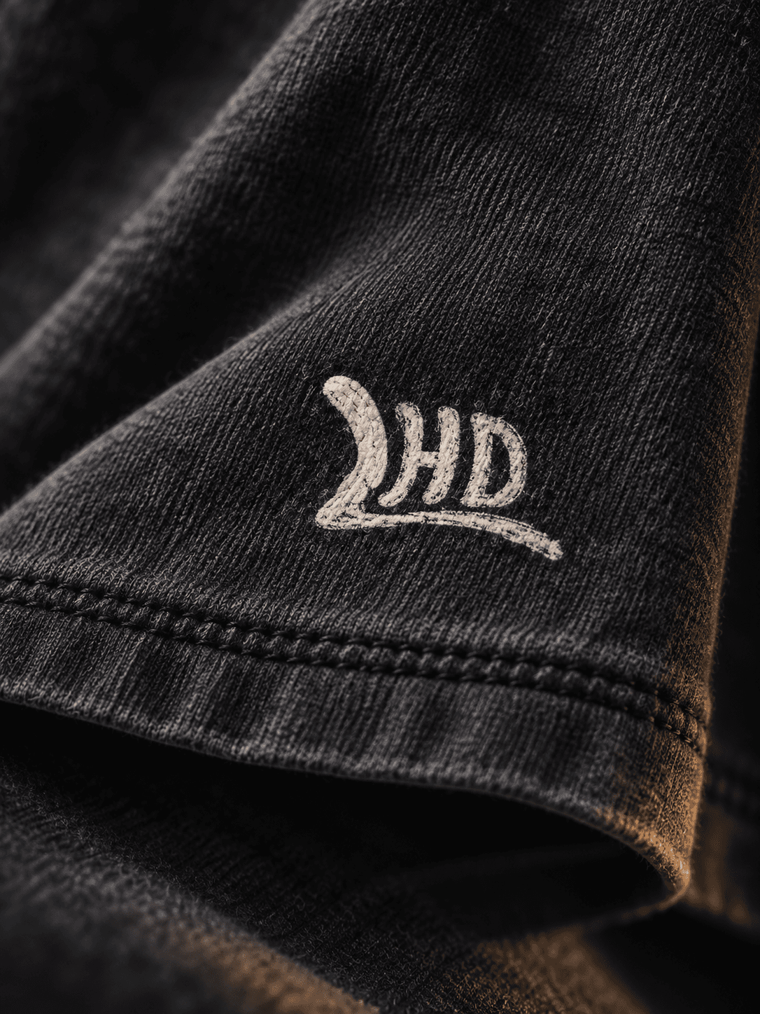 Campaign detail of a pale LHD mark on folds of dark fabric, lit along the hem